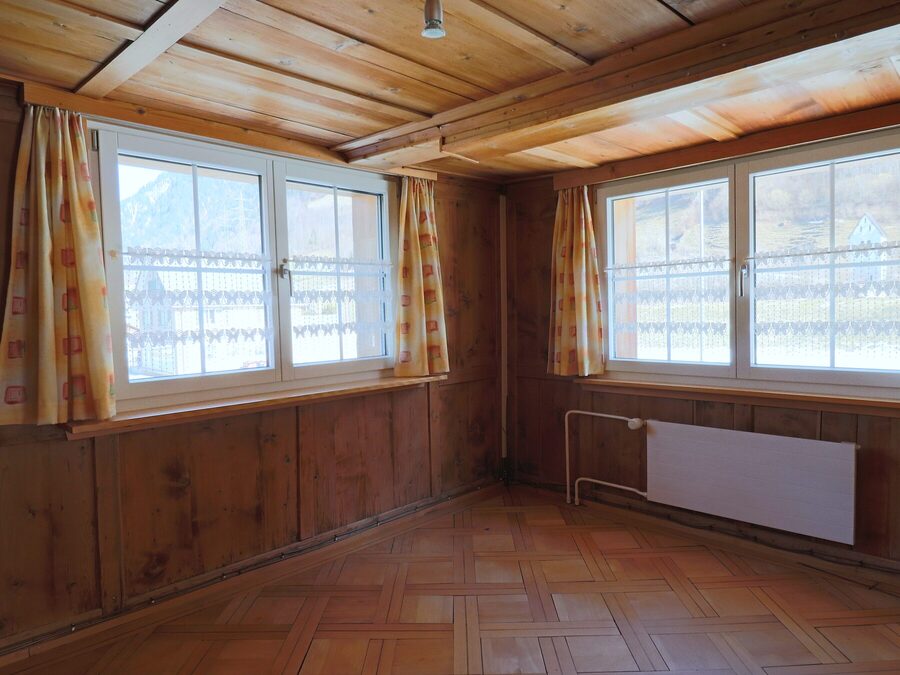 Zimmer mit Mosaikparkett, Täfer und Fenstern auf zwei Seiten